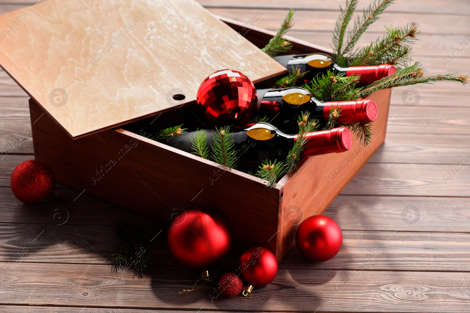 Photo of Wooden crate with bottles of wine, fir twigs and red Christmas balls on table