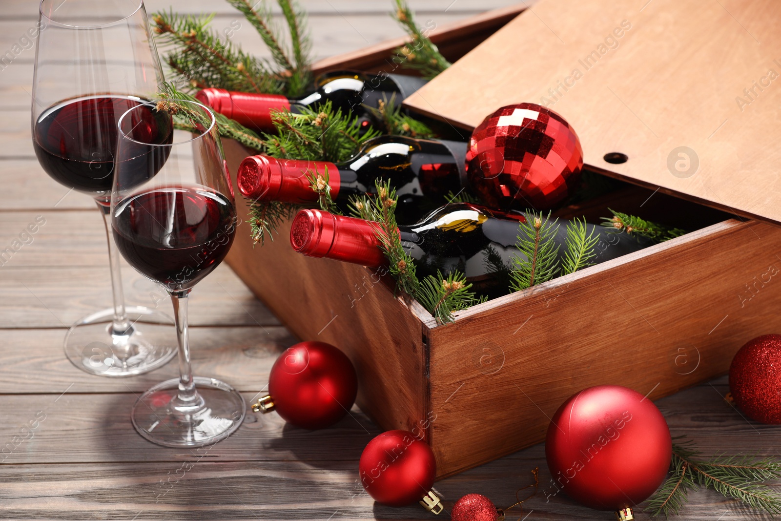 Photo of Wooden crate with bottles of wine, glasses, fir twigs and red Christmas balls on table