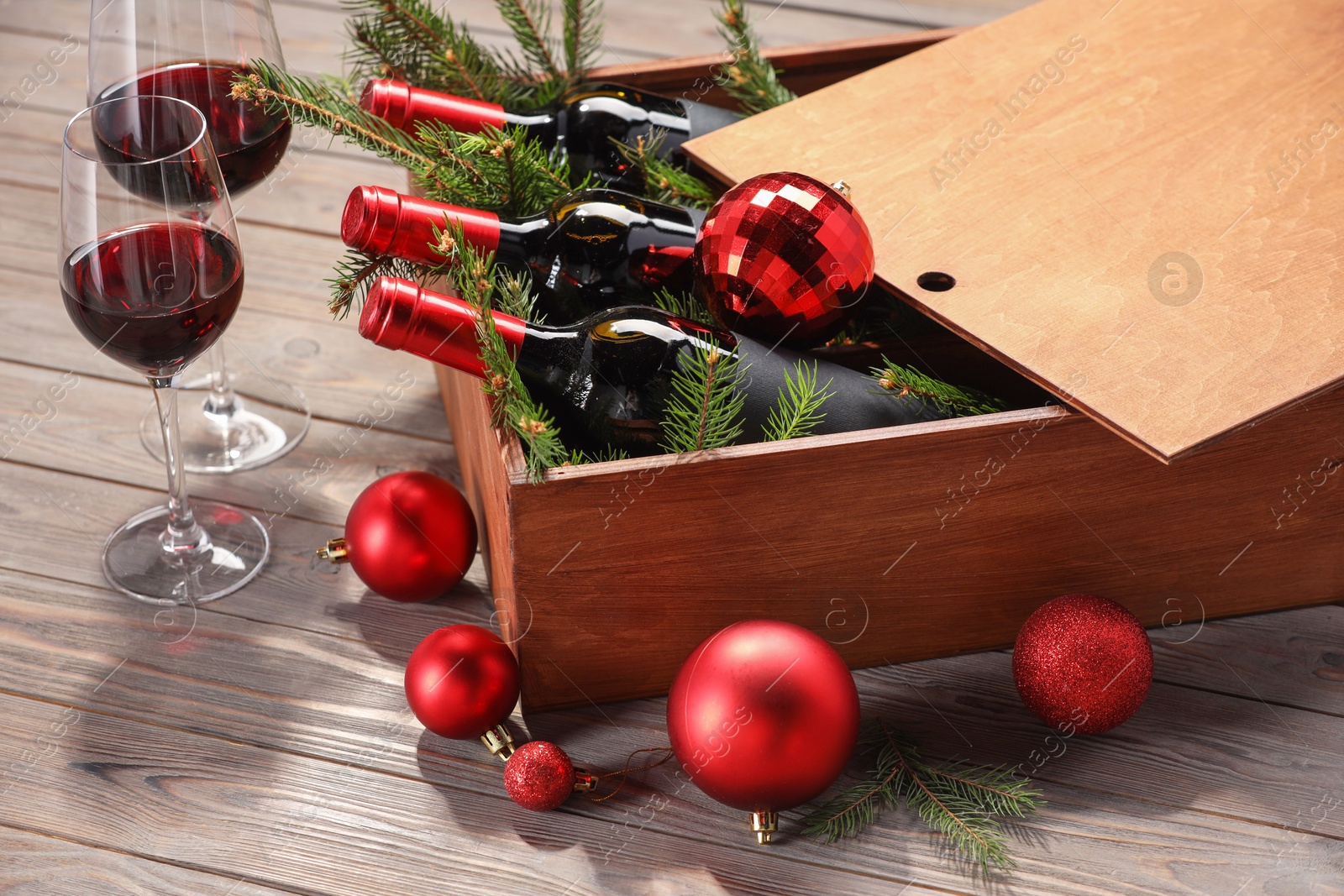 Photo of Wooden crate with bottles of wine, glasses, fir twigs and red Christmas balls on table