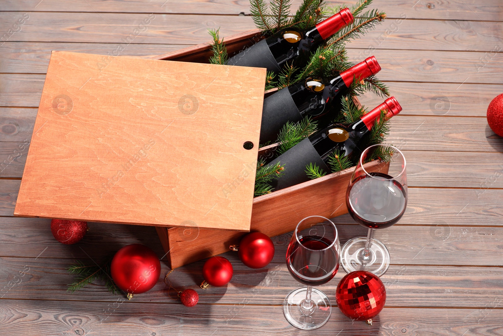 Photo of Wooden crate with bottles of wine, glasses, fir twigs and red Christmas balls on table