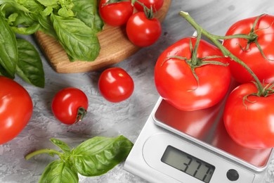 Photo of Kitchen scale with tomatoes and basil on grey textured table, closeup