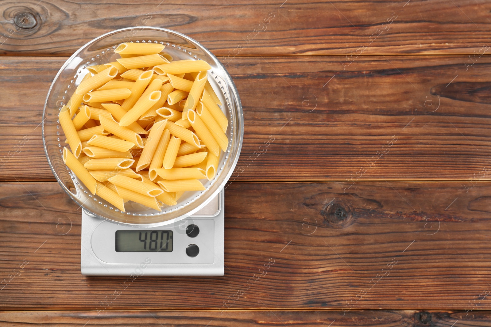 Photo of Kitchen scale with bowl of pasta on wooden table, top view. Space for text