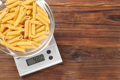 Photo of Kitchen scale with bowl of pasta on wooden table, top view. Space for text