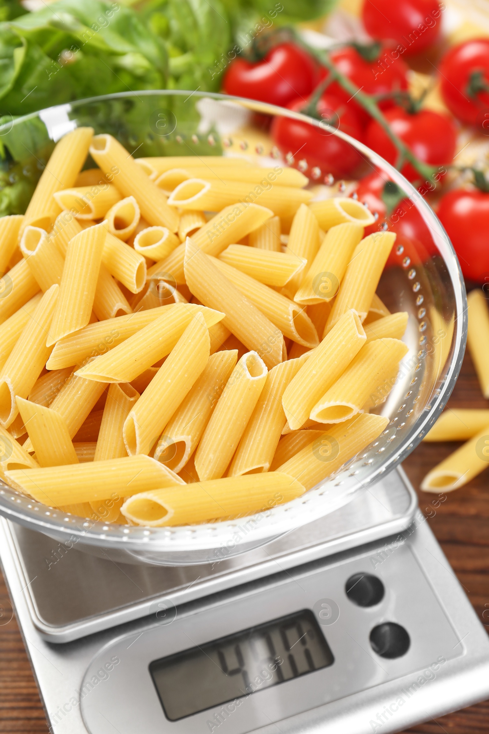 Photo of Kitchen scale with bowl of pasta on wooden table, closeup