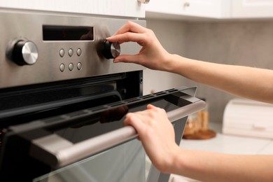 Photo of Woman using electric oven in kitchen, closeup