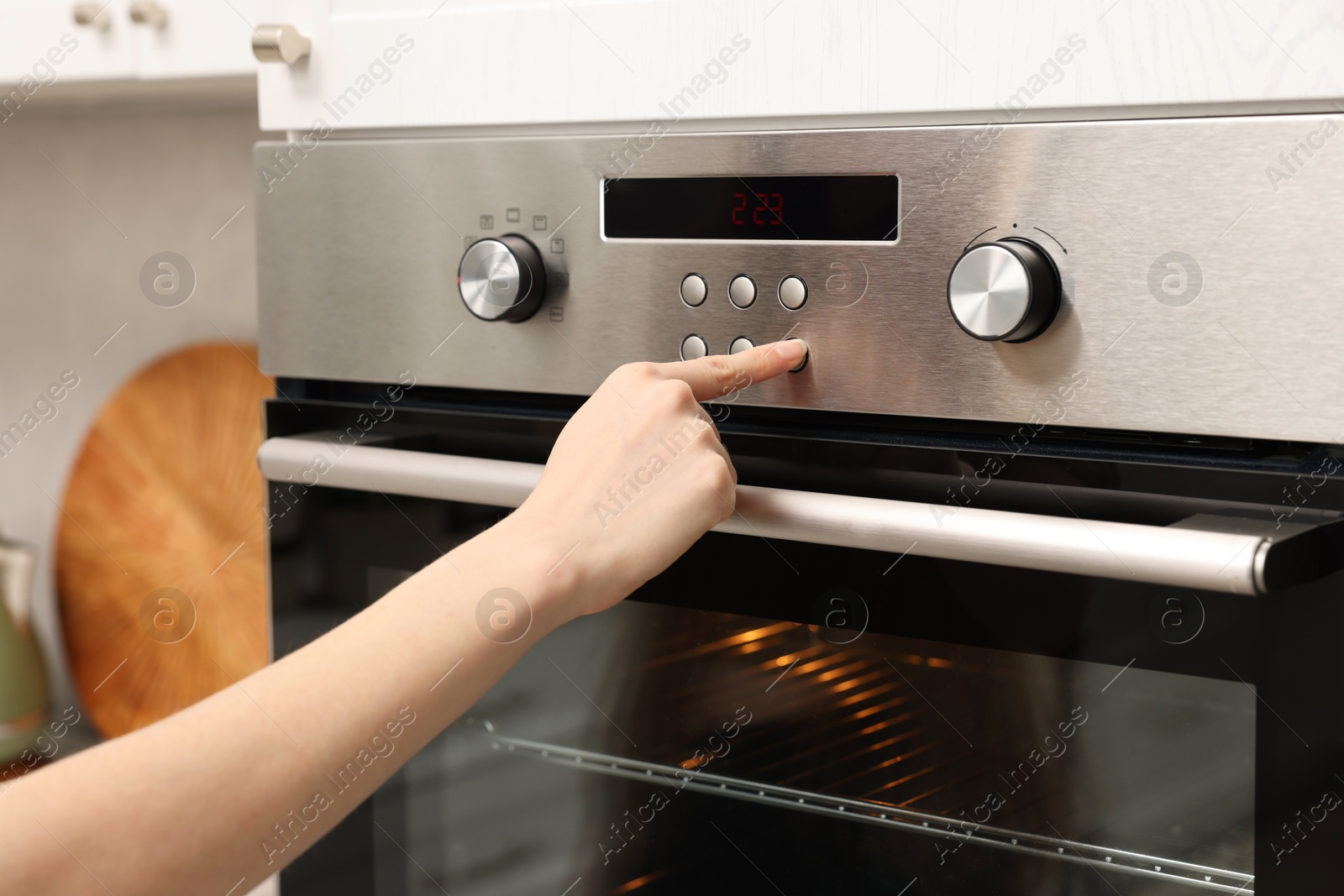 Photo of Woman using electric oven in kitchen, closeup