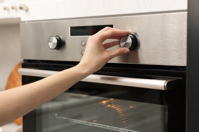 Photo of Woman using electric oven in kitchen, closeup