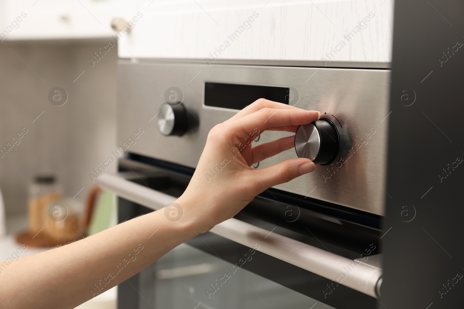 Photo of Woman using electric oven in kitchen, closeup