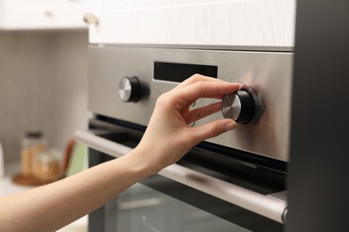 Woman using electric oven in kitchen, closeup