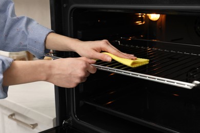 Woman cleaning oven rack with rag in kitchen, closeup