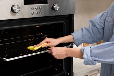 Photo of Woman cleaning oven rack with rag in kitchen, closeup