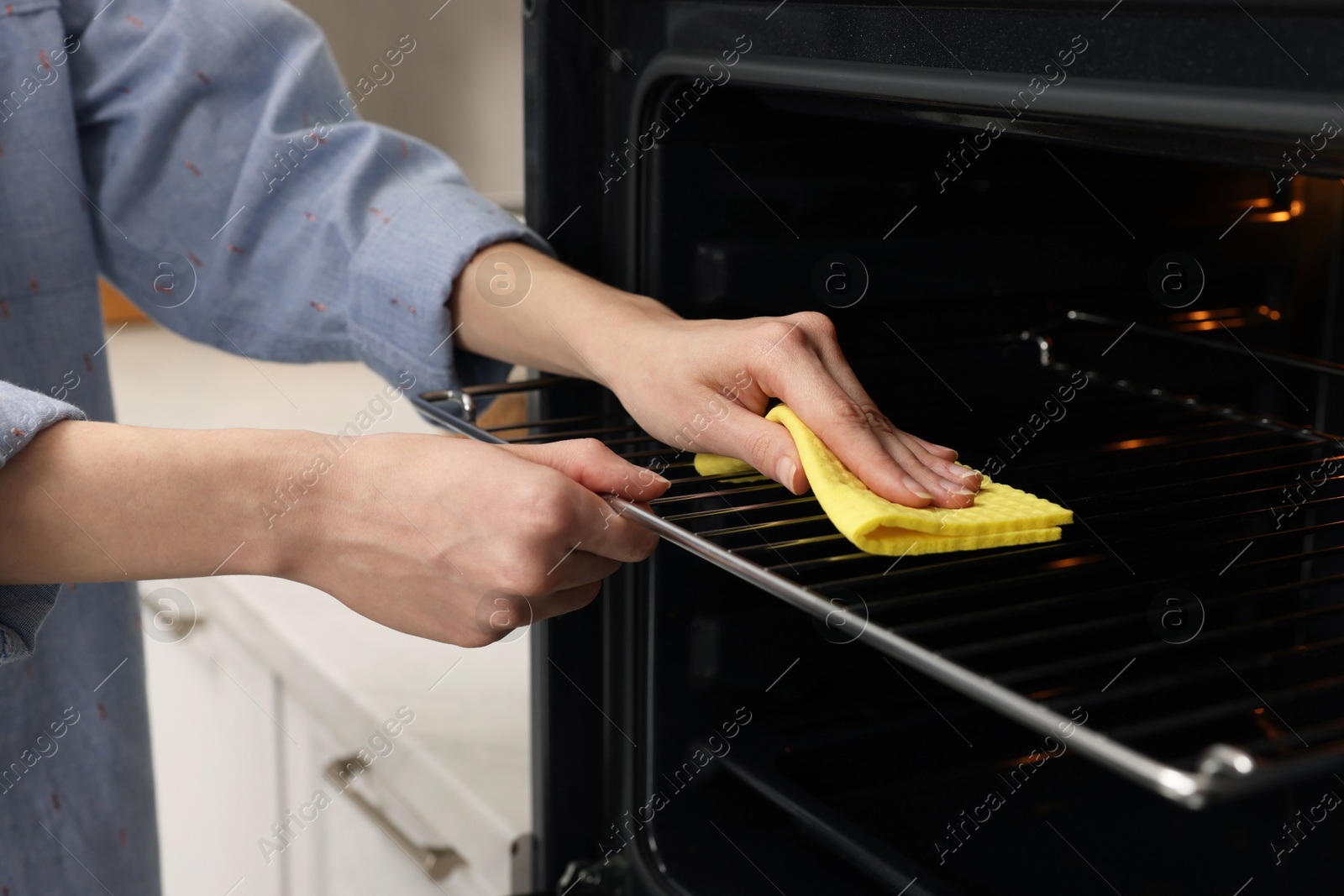 Photo of Woman cleaning oven rack with rag in kitchen, closeup