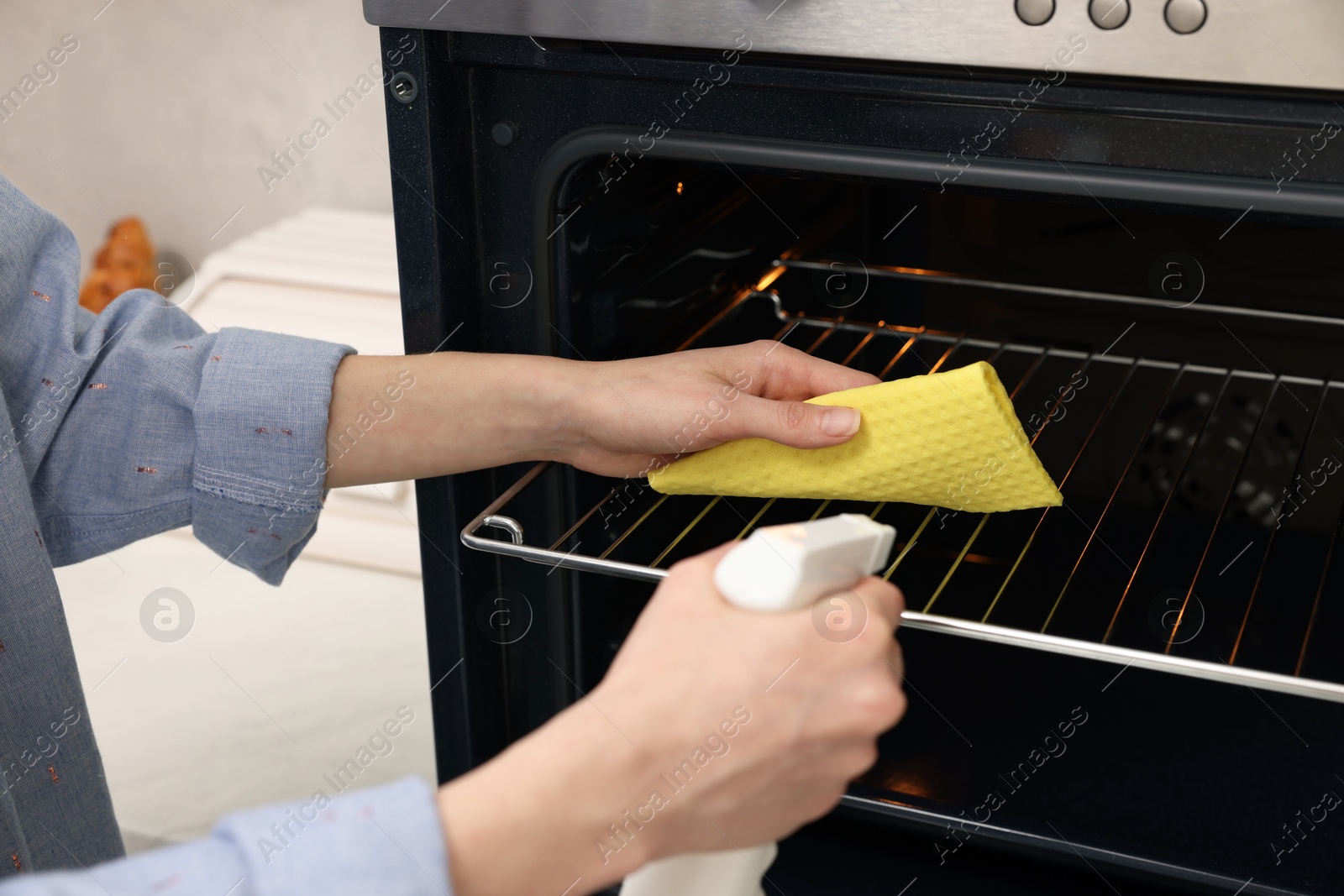 Photo of Woman cleaning oven rack with rag and detergent in kitchen, closeup