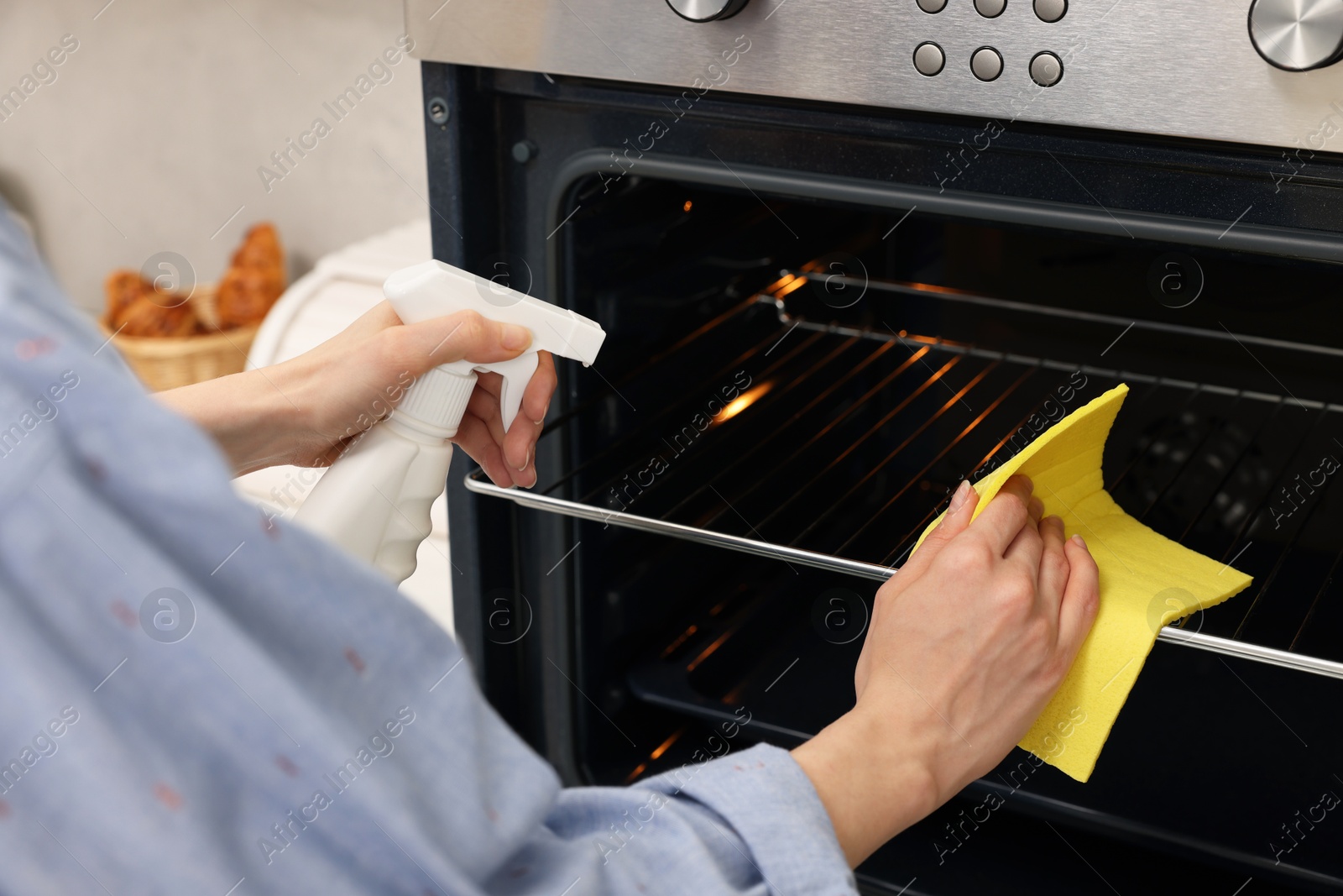 Photo of Woman cleaning oven rack with rag and detergent in kitchen, closeup