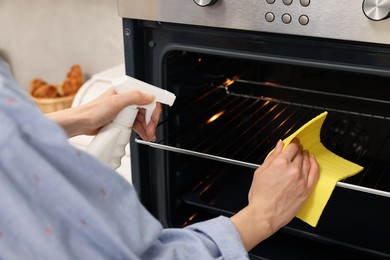 Woman cleaning oven rack with rag and detergent in kitchen, closeup