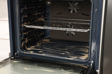 Photo of Open electric oven covered with cleaning foam in kitchen