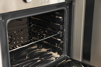 Open electric oven covered with cleaning foam in kitchen