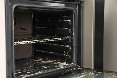 Open electric oven covered with cleaning foam in kitchen