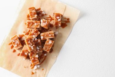 Photo of Tasty candies, caramel sauce and salt on white table, top view. Space for text