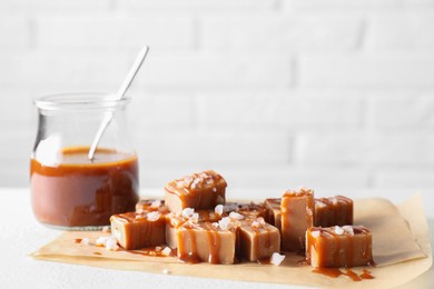 Photo of Tasty candies, caramel sauce and salt on white table