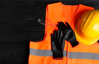 Photo of Reflective vest, hard hat, protective gloves and goggles on black wooden background, top view. Space for text