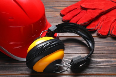 Photo of Hard hat, protective gloves and earmuffs on wooden background, closeup