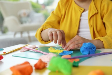 Photo of Little girl sculpting with play dough at table indoors, closeup