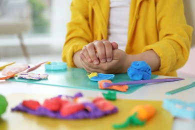 Photo of Little girl sculpting with play dough at table indoors, closeup