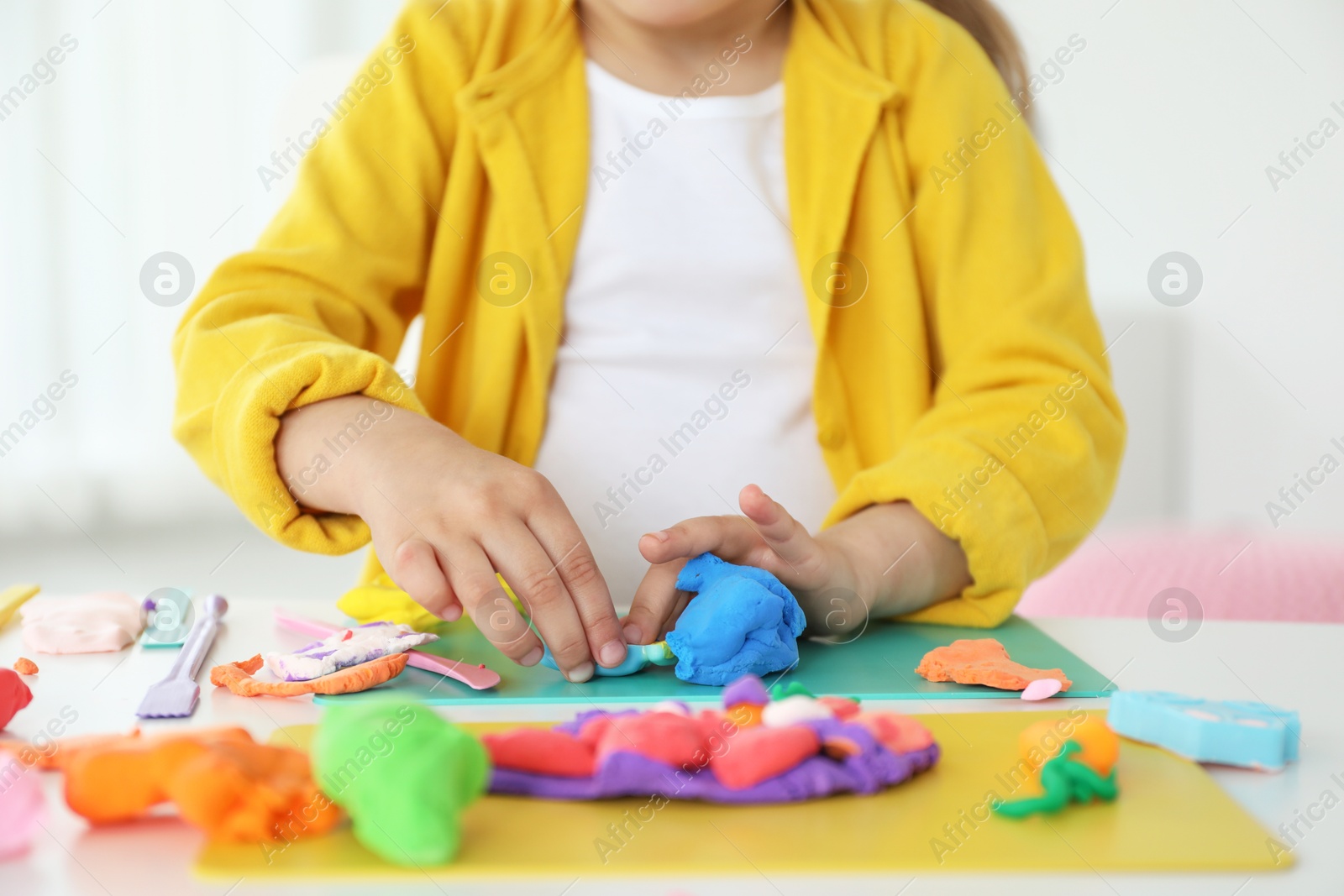 Photo of Little girl sculpting with play dough at white table indoors, closeup