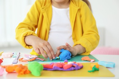 Little girl sculpting with play dough at white table indoors, closeup