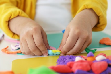 Photo of Little girl sculpting with play dough at white table indoors, closeup