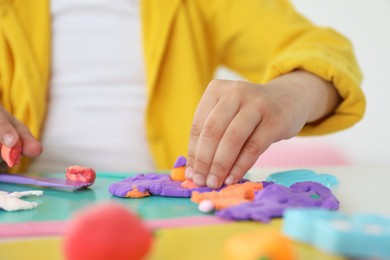 Little girl sculpting with play dough at table indoors, closeup