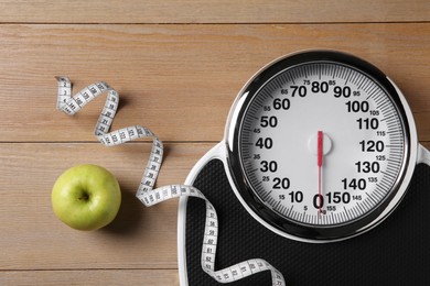 Photo of Scale, measuring tape and fresh apple on wooden floor, flat lay