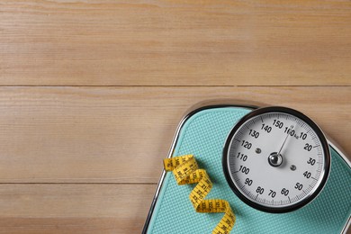 Photo of Scale and measuring tape on wooden floor, top view. Space for text