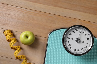 Photo of Scale, measuring tape and fresh apple on wooden floor, flat lay