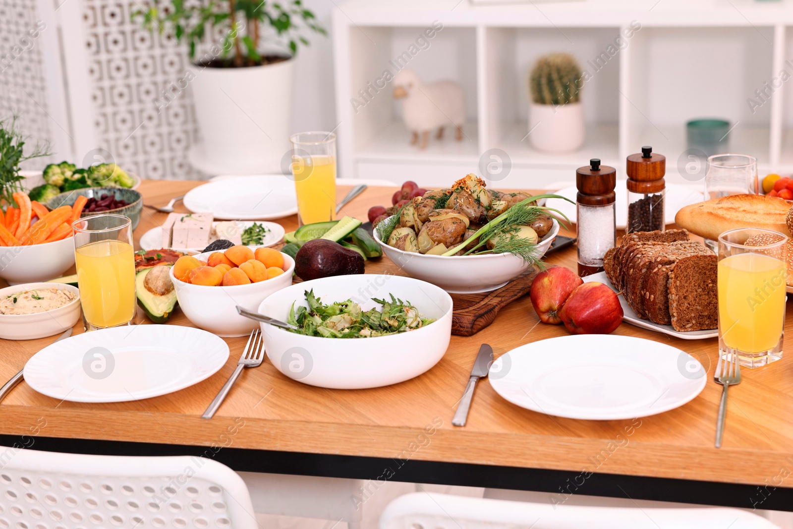 Photo of Healthy vegetarian food, glasses of juice, cutlery and plates on wooden table indoors