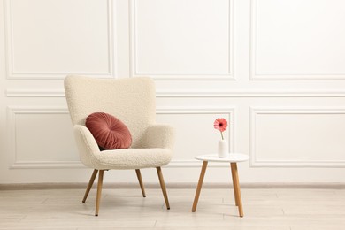 Soft armchair and coffee table with flower in stylish room