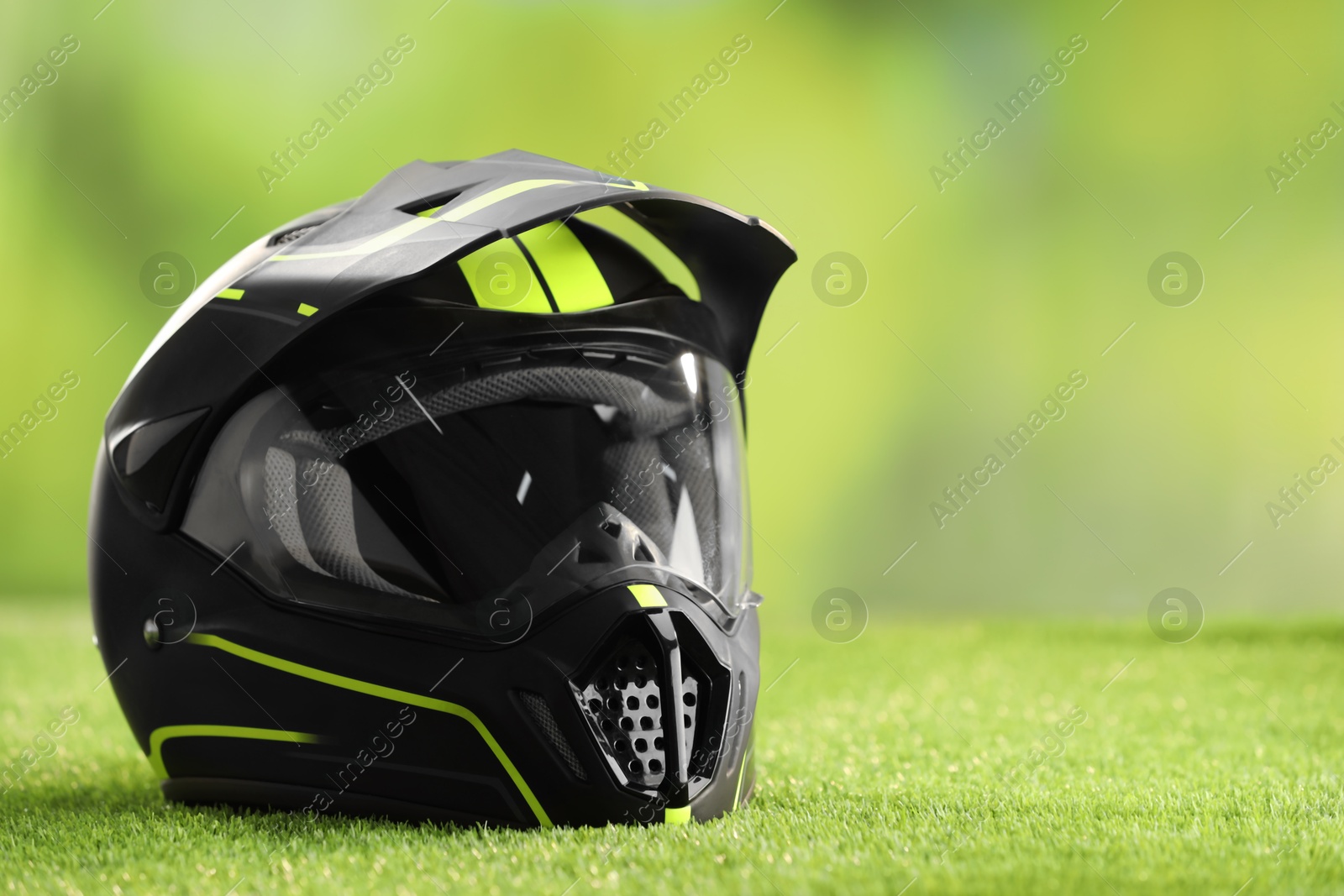 Photo of Modern motorcycle helmet with visor on green grass, space for text