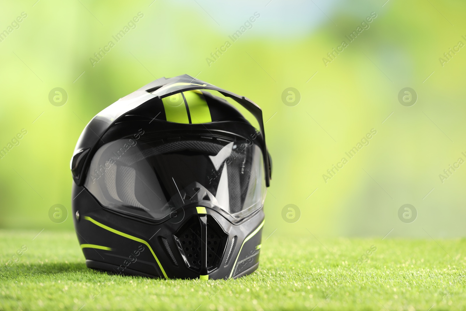 Photo of Modern motorcycle helmet with visor on green grass, space for text