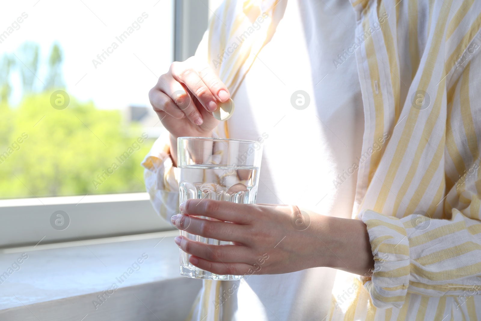 Photo of Woman putting effervescent pill into glass of water indoors, closeup