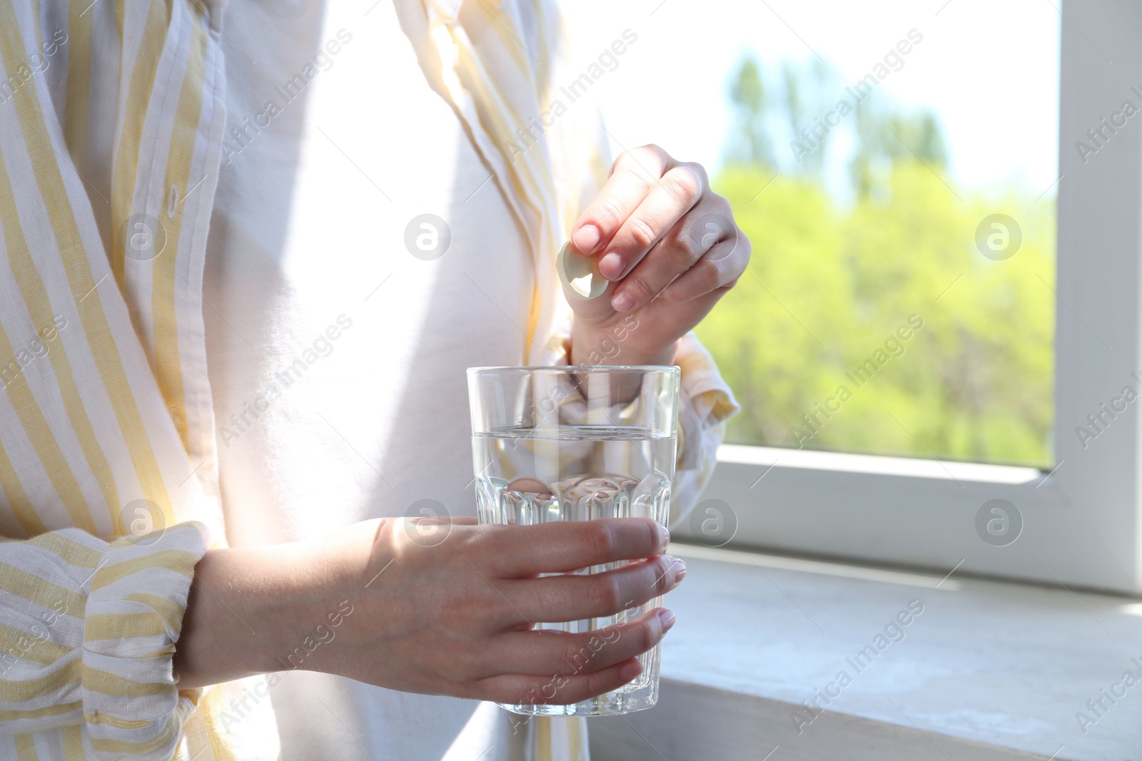 Photo of Woman putting effervescent pill into glass of water indoors, closeup