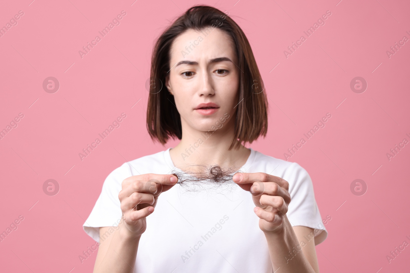 Photo of Sad woman holding clump of lost hair on pink background. Alopecia problem