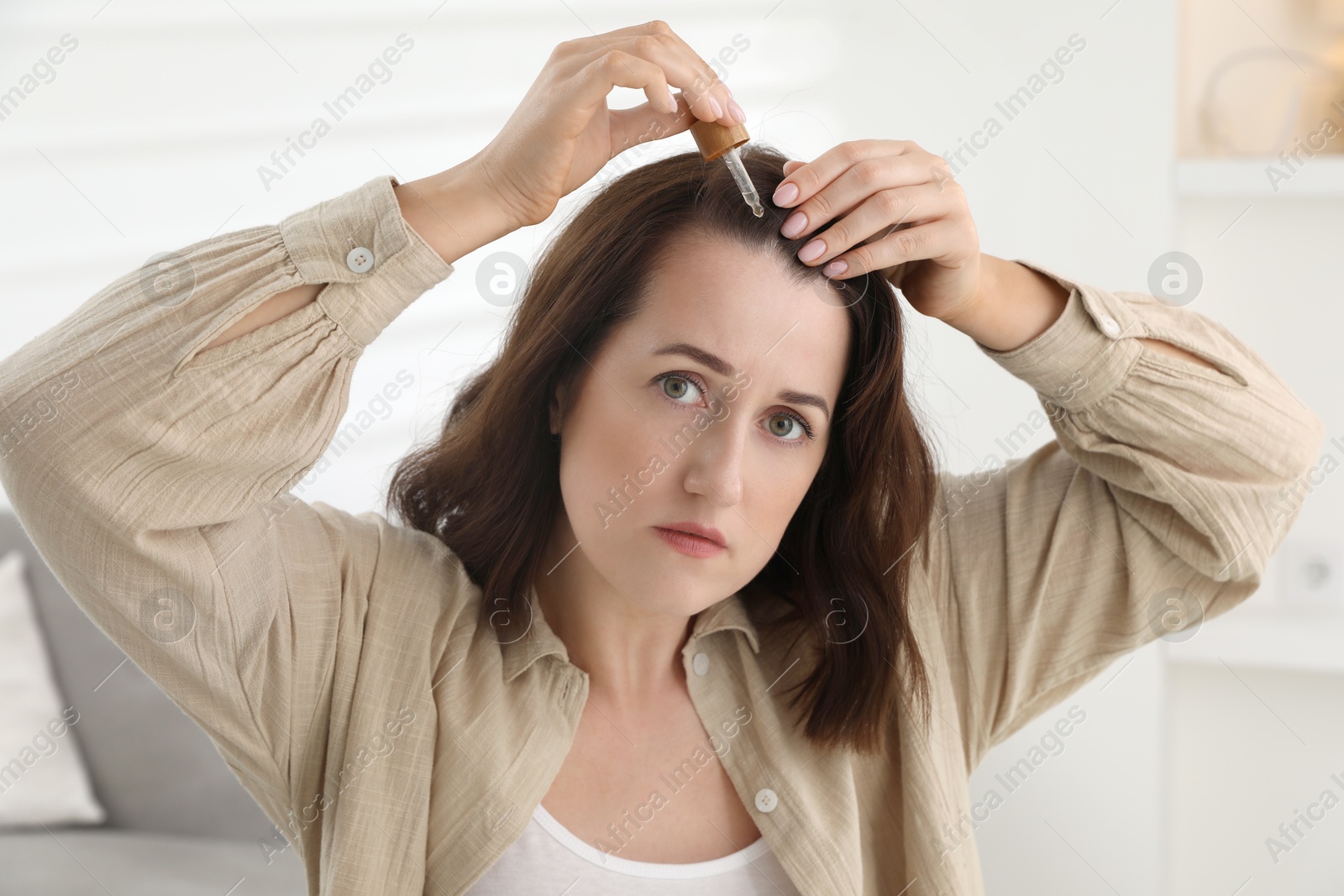 Photo of Hair loss problem. Woman applying serum onto hairline indoors