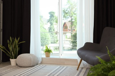 Photo of Sofa, green houseplants, pouffe and elegant curtains in room. Interior design