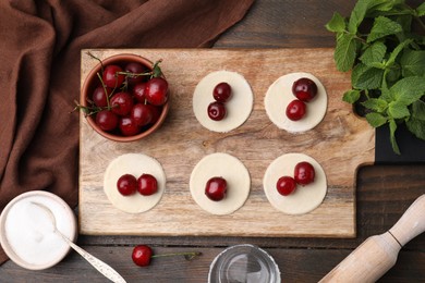 Photo of Process of making dumplings (varenyky) with cherries. Raw dough and ingredients on wooden table, flat lay