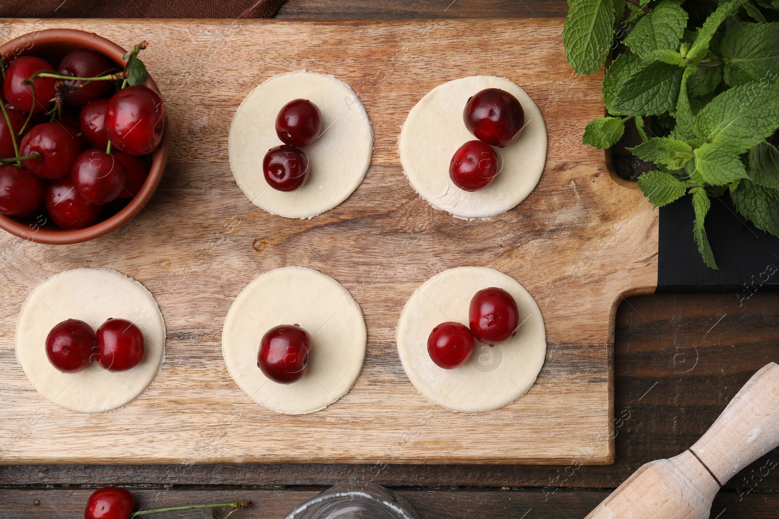 Photo of Process of making dumplings (varenyky) with cherries. Raw dough and ingredients on wooden table, flat lay