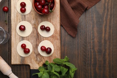 Process of making dumplings (varenyky) with cherries. Raw dough and ingredients on wooden table, flat lay. Space for text