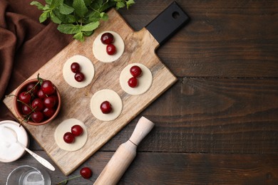 Process of making dumplings (varenyky) with cherries. Raw dough and ingredients on wooden table, flat lay. Space for text