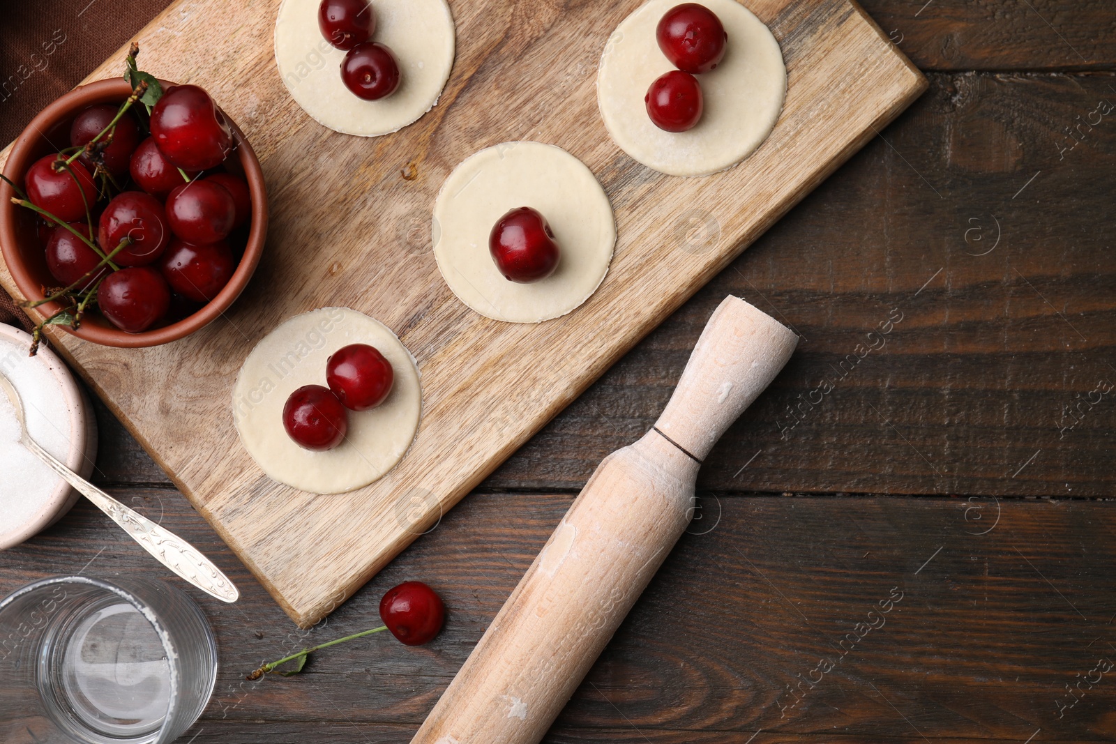 Photo of Process of making dumplings (varenyky) with cherries. Raw dough and ingredients on wooden table, flat lay