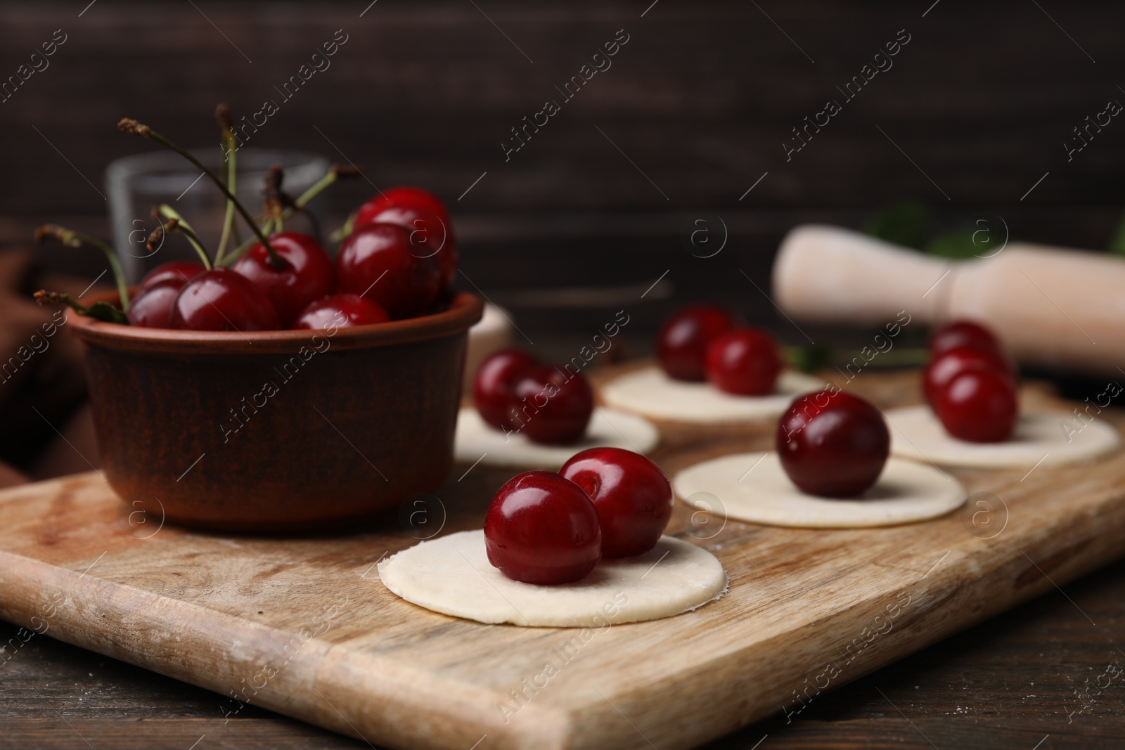 Photo of Process of making dumplings (varenyky) with cherries. Raw dough and ingredients on wooden table, closeup